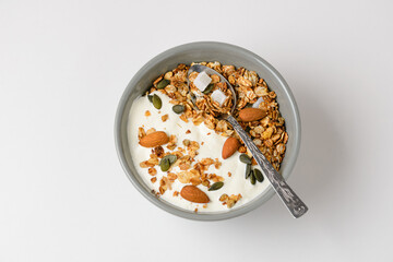 Top view of the traditional morning dish granola with almonds, pumpkin seeds, coconut, dried oat flakes and other cereals with yogurt in a gray bowl with a spoon