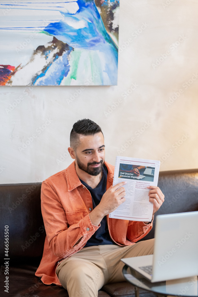 Poster confident young man pointing at financial paper while sitting in front of laptop and explaining info