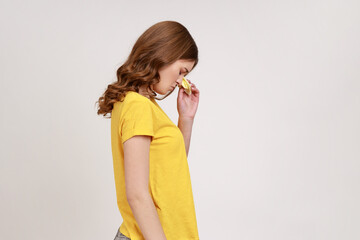 Profile portrait of teenager girl with wavy hair in yellow T-shirt expressing sadness and depression, upset female crying, desperate sorrowful feelings. Indoor studio shot isolated on gray background.