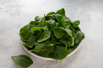 Fresh spinach leaves in a bowl on gray background. Healthy food ingredient