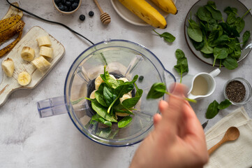 Cooking, preparring green spinach, banana and blueberry smoothie. Female hands, top view. Step by step recipe.