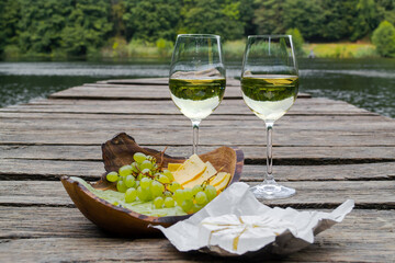 Picnic at the wooden pier by the lake with food, fruit and white wine. Picnic for two, romantic outdoor recreation