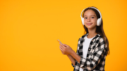 Side view caucasian teenager schoolgirl pupil student listening to her favorite music song singer rockband in headphones using mobile application on her phone isolated in yellow background