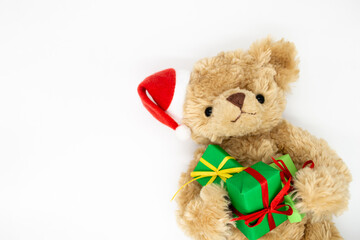 A stuffed toy Teddy bear in a red Santa Claus hat with a pompom on one ear, holding green gift boxes in its paws. White background, copy space. The concept of Christmas gifts, sales