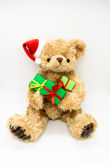 Vertical photo with stuffed toy Teddy bear in a red Santa Claus hat with a pompom on one ear, holding green gift boxes in its paws. White background, copy space. The concept of Christmas gifts, sales