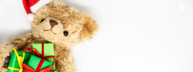 Banner with stuffed toy Teddy bear in a red Santa Claus hat with a pompom on one ear, holding green gift boxes in its paws. White background, copy space. The concept of Christmas gifts, sales