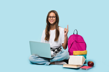 Sitting full-length teenager schoolgirl with laptop computer showing pointing on copy space having idea, surfing webpages on Internet,social media,e-learning remotely isolated in blue background - obrazy, fototapety, plakaty
