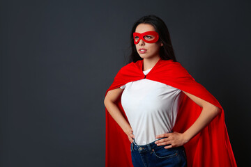 Confident young woman wearing superhero cape and mask on grey background, space for text