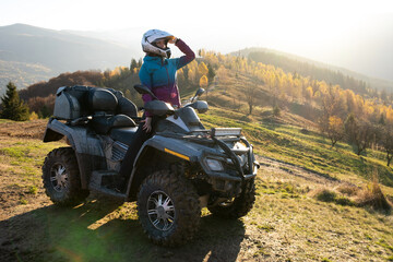 Young happy female driver in protective helmet enjoying extreme ride on ATV quad motorbike in fall...