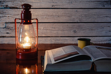 Lámpara de vela antigua junto a un libro abierto, concepto de apagón eléctrico - obrazy, fototapety, plakaty