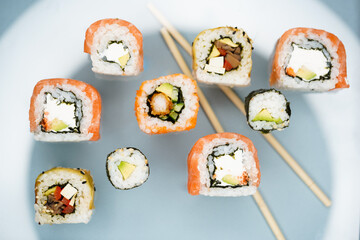 a mix of different types of sushi with fish and vegan with vegetables on a light background in a beautiful original light on a background of blurry sushi sticks