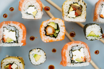 a mix of different types of sushi with fish and vegan with vegetables on a light background in a beautiful original light on a background of blurry sushi sticks
