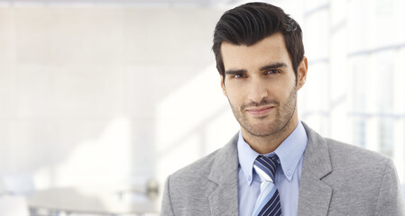 Confident businessman smiling in modern business office. Portrait of young adult man in 30s, happy confident smile. Copy space.