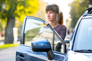 Young woman driver enjoying warm summer day standing beside her car on city street. Travelling and vacation concept.