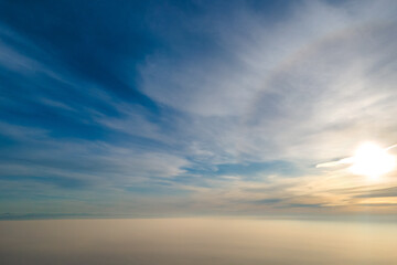 Aerial view of vibrant yellow sunrise over white dense clouds with blue sky overhead.