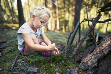 Little girl is building small house made of sticks. Child is playing in forrest.