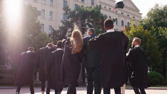 In the college garden graduates students multiracial throw up the graduation caps after the end of graduation taking video from the back at the end they hugging each other