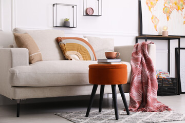 Stylish ottoman with books and cup of coffee near sofa in light living room