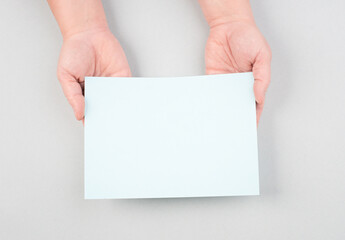 Woman holds a blank sheet of paper, grey colored background, empty copy space for text, minimalism
