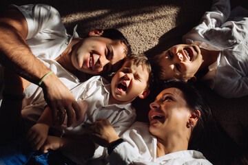 Happy family dressed in jeans and white shirts lie on the floor and laugh together in sunlight. 