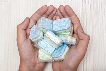 Hands holding many green and blue dishwasher soap tablets in water-soluble packaging
