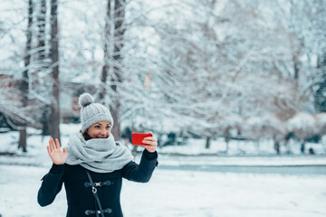 Woman using a smartphone and wearing scarf and a a hat on a cold winter day