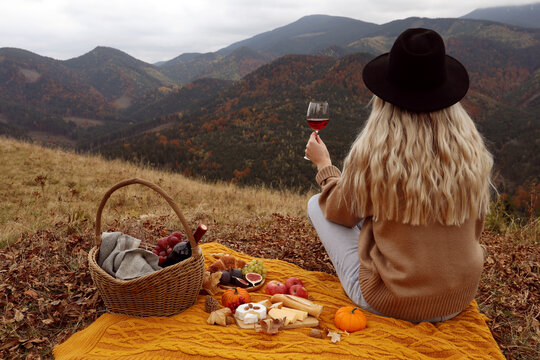 Young woman with glass of wine having picnic in mountains on autumn day, back view. Space for text