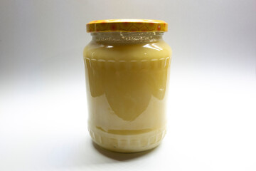 Fresh honey from bee plastic in a glass bottle with a cap on a light background.