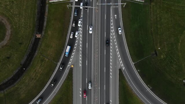 Automobiles and lorries drive along marked multilevel overpass highway with fork and grassy lanes on gloomy day aerial view