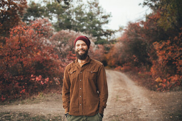 Young man hipster with long beard wearing stylish clothes having a walk in autumn forest.