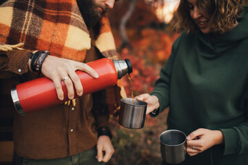 Fototapeta premium Happy couple in love drinking tea from thermos in beautiful autumn forest.
