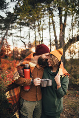 Happy couple in love drinking tea from thermos in beautiful autumn forest.