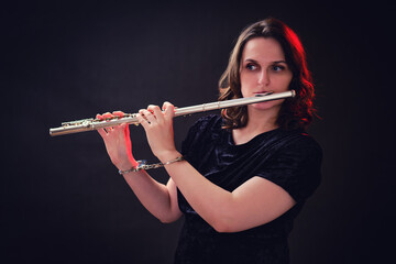 Woman musician with a flute in handcuffed hands on a studio dark background. Problems of musical playing at concerts, the concept of non-freedom and arrests