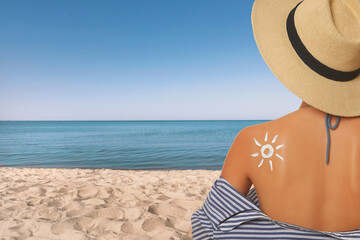 Young woman with sun protection cream on sandy beach, space for text