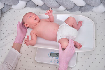 The doctor weighs a newborn baby on a scale. Uniformed nurse taking measurements of the child weight