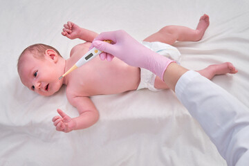 Doctor checks the temperature of the newborn baby with a thermometer. A nurse in uniform measures the child fever with a thermometer