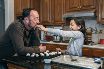 Girl feeding dad Christmas cookie in kitchen