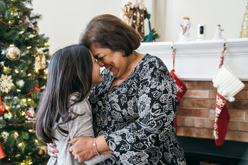 Girl hugging and touching foreheads with grandma in front of Christmas tree