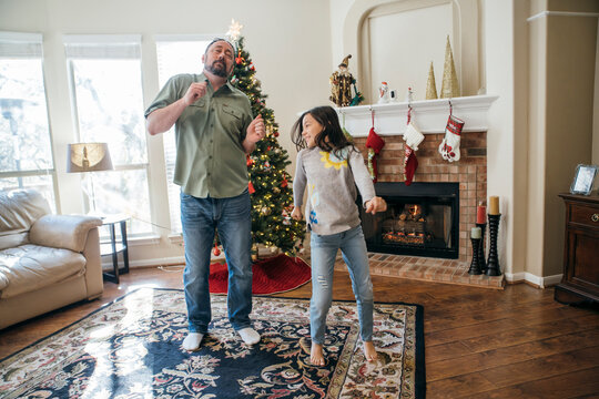 Dad And Daughter Dancing In Living Room In Front Of Christmas Tree And Fireplace