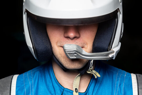 Full face portrait of a racing driver in a gray helmet. The eyes are hidden. Blue clothes, Black background