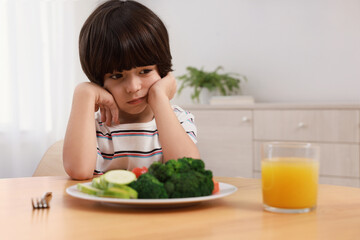 Cute little boy refusing to eat vegetables at home