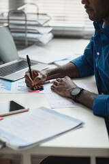 Side view close up of young African-American man working at desk in office and writing notes, copy...