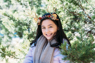Portrait of smiling girl in winter coat and scarf outside in forest wearing headband with flowers and branches