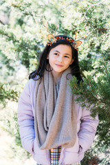 Girl in winter coat and scarf standing outside in forest wearing headband with flowers and branches looking up