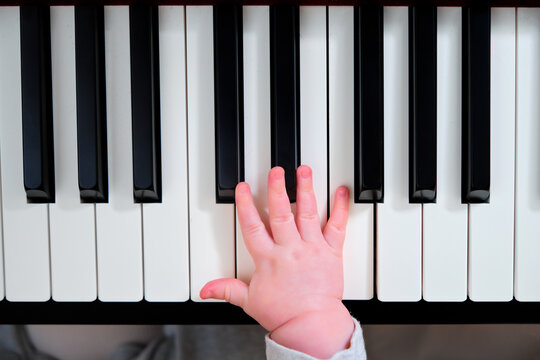 A small child hand on the piano keys, close-up. Infant baby plays the electronic piano