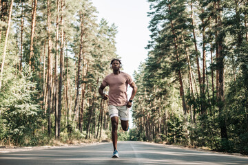 African American man, runner running on trail in the forest,Man with headphones running in the park in the morning,