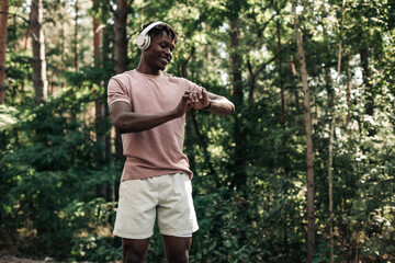 Male runner, American man checking fitness progress on his smartwatch while walking in the woods in nature