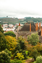 Fototapeta na wymiar Palace in the autumn yellow orange and green forest with cloudy sky atmosphere of fall city in the background - Palace of Dukes in Guimaraes, Portugal