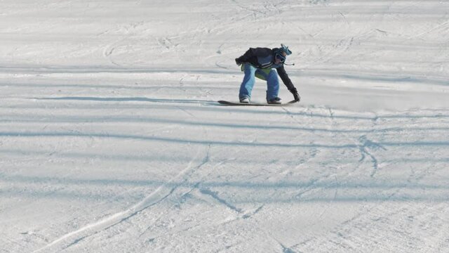 Snowboarder technically carves down the hill and performs buttering tail grab trick. A frosty sunny winter day on a slope at a ski resort.