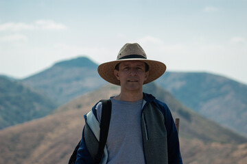 man in the mountains wearing a hat. Mountains at the background - obrazy, fototapety, plakaty